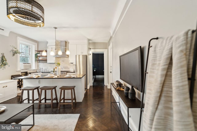 kitchen featuring tasteful backsplash, dark countertops, an inviting chandelier, white cabinets, and wall chimney range hood