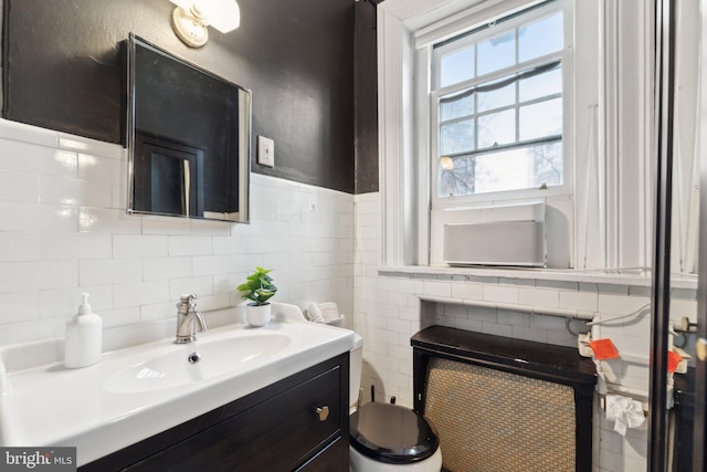 half bathroom featuring toilet, a wainscoted wall, vanity, and tile walls