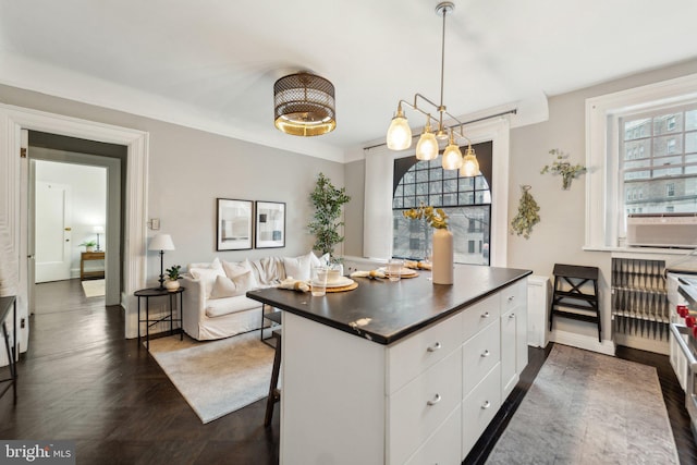 kitchen with a breakfast bar area, a kitchen island, white cabinetry, hanging light fixtures, and dark countertops