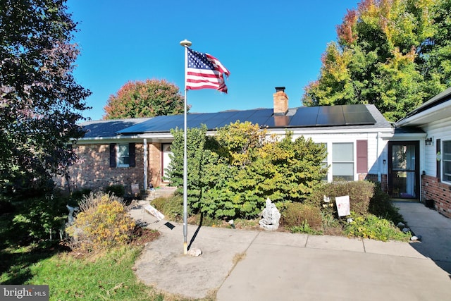 single story home with brick siding, a chimney, and roof mounted solar panels