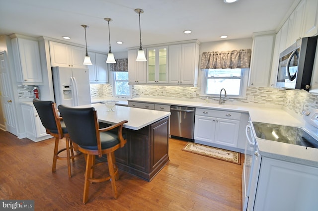 kitchen with a kitchen island, wood finished floors, stainless steel appliances, light countertops, and white cabinetry