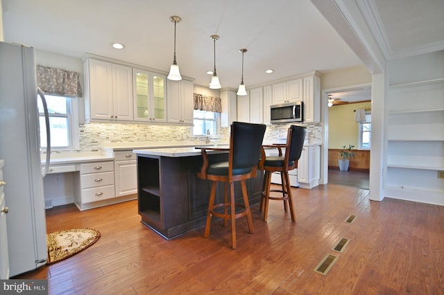 kitchen with wood finished floors, white cabinetry, light countertops, freestanding refrigerator, and stainless steel microwave