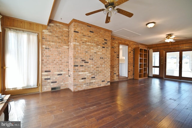 unfurnished living room featuring a ceiling fan, brick wall, visible vents, and wood finished floors