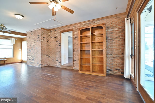 unfurnished living room with ceiling fan, brick wall, dark wood-type flooring, and attic access