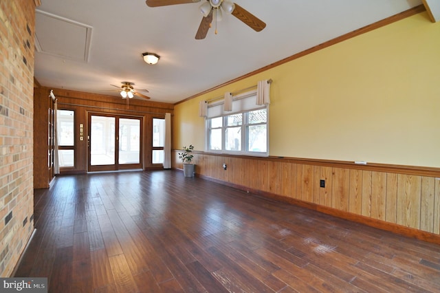 unfurnished room featuring attic access, wooden walls, a wainscoted wall, ornamental molding, and dark wood-type flooring