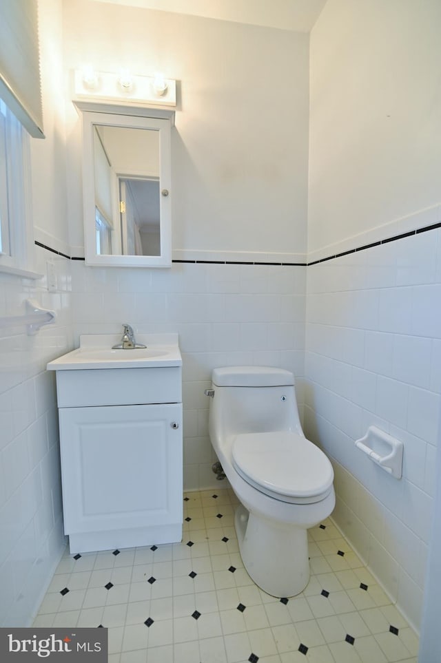 half bathroom with tile walls, a wainscoted wall, vanity, and toilet