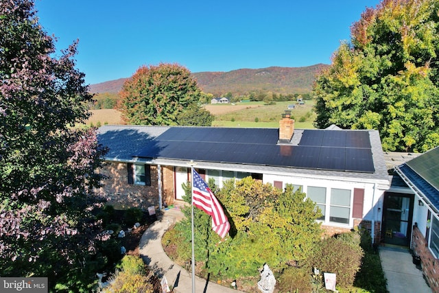 view of front facade featuring brick siding, a chimney, a mountain view, and roof mounted solar panels