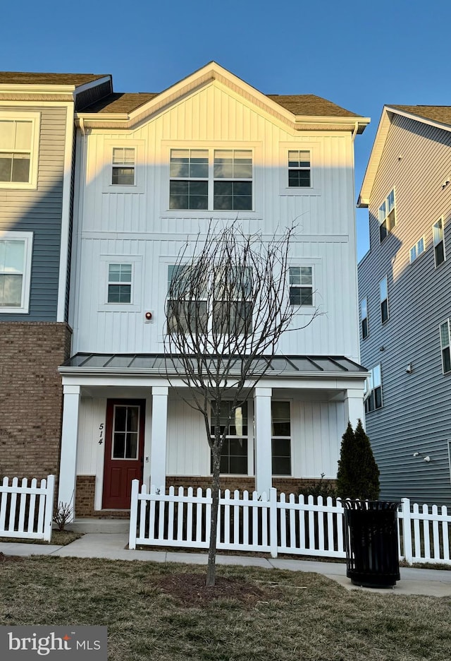 view of front of home featuring a standing seam roof, board and batten siding, covered porch, and a fenced front yard