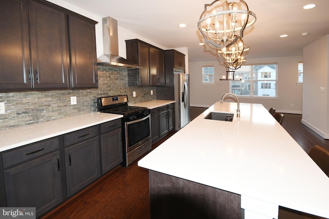 kitchen featuring dark wood finished floors, an inviting chandelier, appliances with stainless steel finishes, a sink, and wall chimney range hood