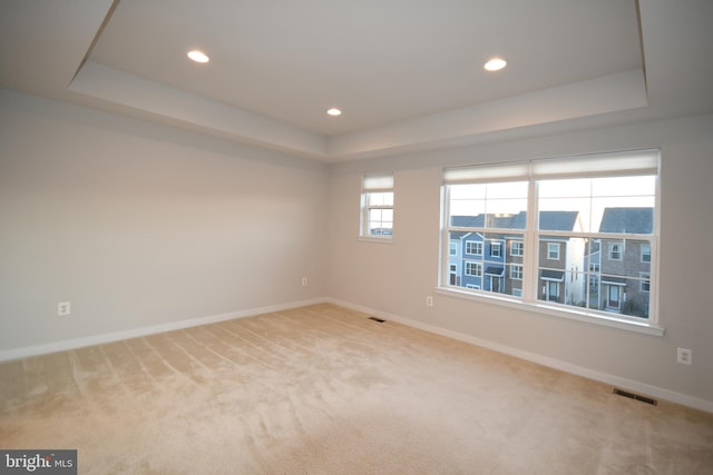 carpeted spare room with a raised ceiling, visible vents, and baseboards