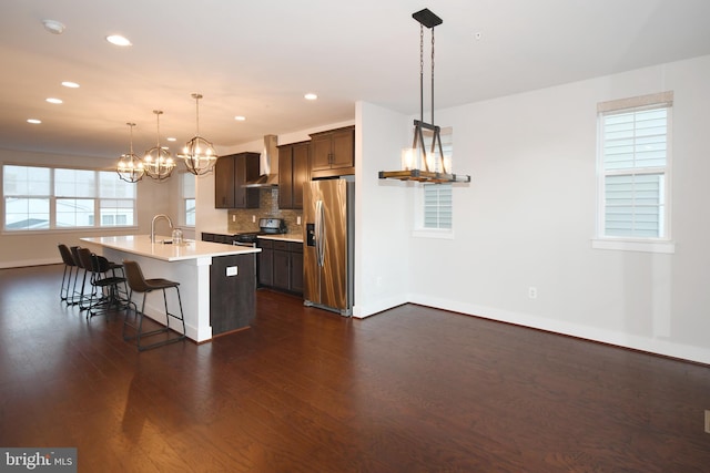 kitchen with wall chimney exhaust hood, appliances with stainless steel finishes, dark wood-type flooring, light countertops, and a kitchen bar