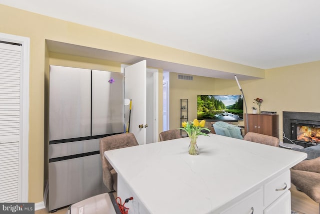 kitchen featuring visible vents, open floor plan, white cabinets, a kitchen island, and a lit fireplace