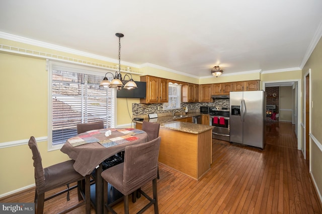 kitchen with stainless steel appliances, a peninsula, dark wood-style flooring, backsplash, and brown cabinets