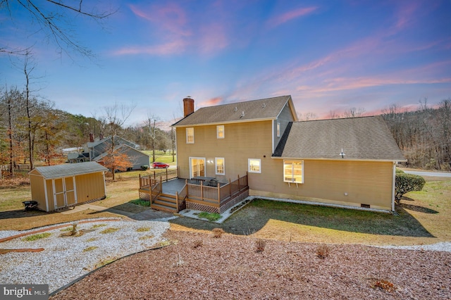 rear view of property with a storage shed, a shingled roof, a chimney, an outbuilding, and a wooden deck