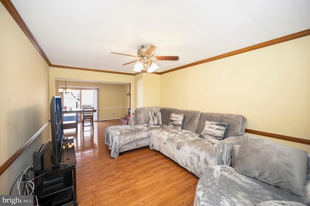 living room featuring ornamental molding, light wood-style flooring, baseboards, and ceiling fan with notable chandelier