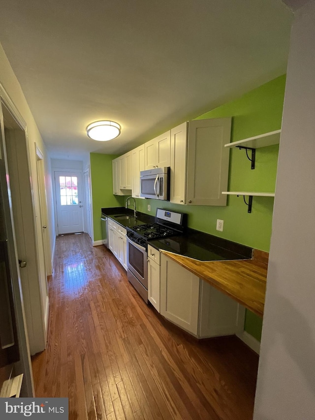 kitchen featuring dark wood finished floors, stainless steel appliances, white cabinetry, open shelves, and a sink