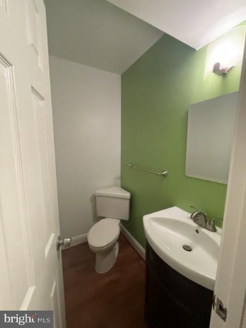 half bathroom with baseboards, vanity, toilet, and wood finished floors