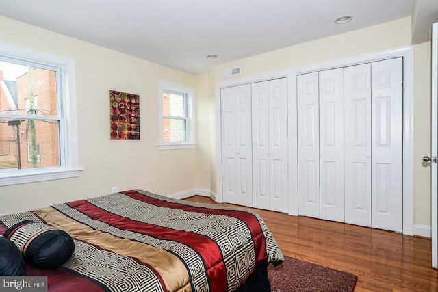 bedroom with two closets, baseboards, visible vents, and wood finished floors