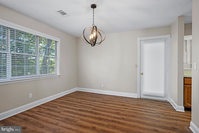 spare room featuring dark wood-style flooring, visible vents, a notable chandelier, and baseboards