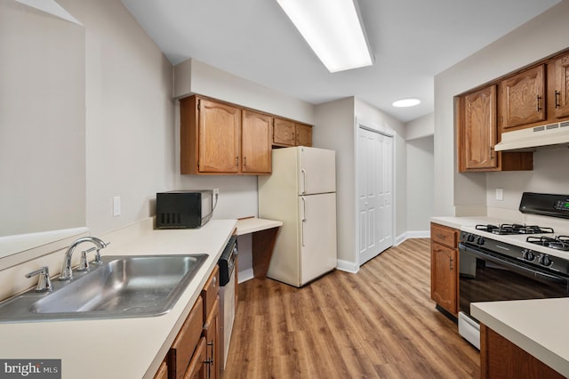 kitchen featuring freestanding refrigerator, a sink, gas range, black microwave, and under cabinet range hood