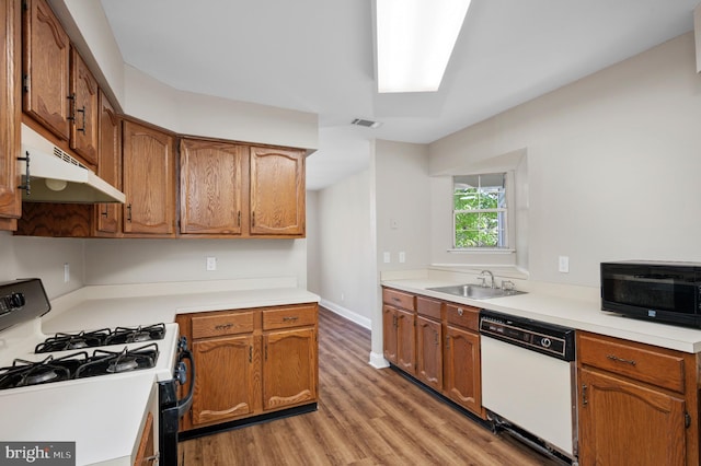 kitchen featuring white dishwasher, under cabinet range hood, a sink, light wood-type flooring, and gas range oven