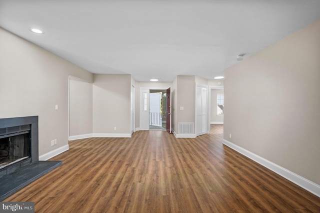 unfurnished living room featuring a fireplace with raised hearth, wood finished floors, visible vents, and baseboards