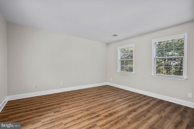 unfurnished room with wood finished floors, visible vents, and baseboards