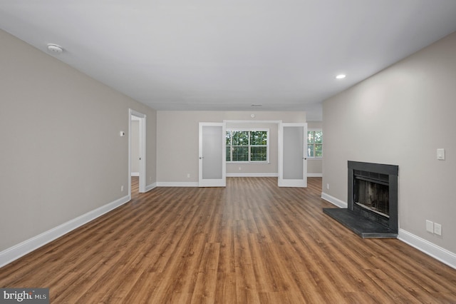 unfurnished living room featuring baseboards, a fireplace with raised hearth, wood finished floors, and recessed lighting