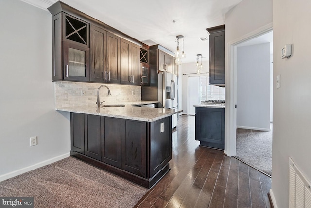 kitchen featuring visible vents, dark brown cabinets, glass insert cabinets, decorative backsplash, and a sink