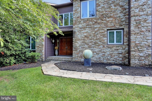 view of exterior entry with stone siding and a lawn