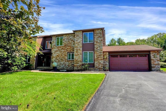 view of front of house featuring an attached garage, stone siding, driveway, and a front yard