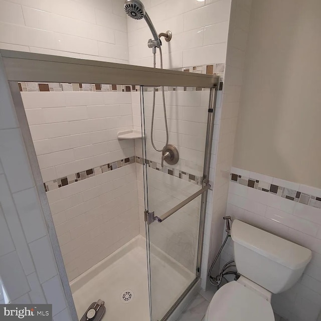 full bathroom featuring a stall shower, toilet, tile walls, and a wainscoted wall