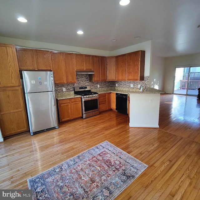 kitchen featuring appliances with stainless steel finishes, under cabinet range hood, brown cabinetry, light wood-style flooring, and recessed lighting