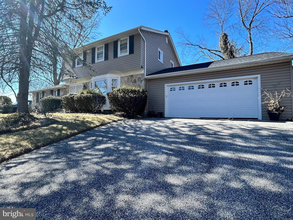 view of front facade featuring stone siding, an attached garage, and driveway