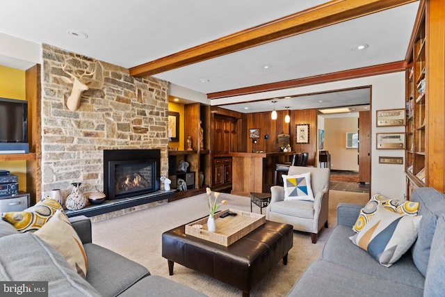 living area featuring a stone fireplace, carpet flooring, beam ceiling, and wooden walls