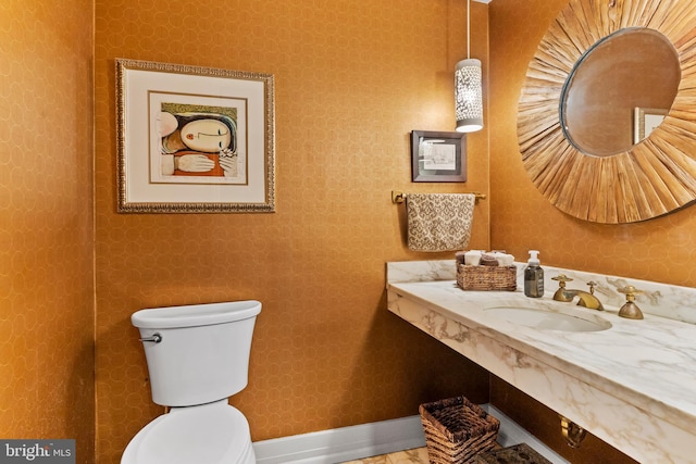 bathroom with baseboards, a sink, toilet, and wallpapered walls