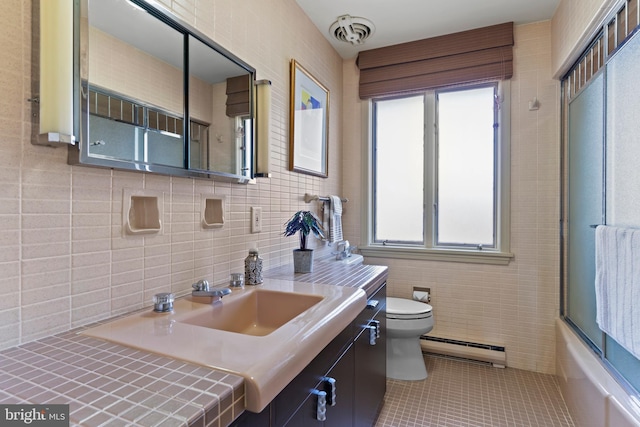 full bathroom with tile walls, toilet, a baseboard heating unit, vanity, and tile patterned floors