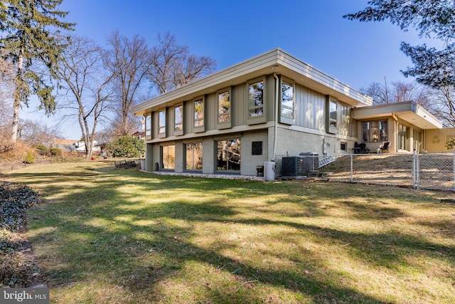 back of house with central AC unit, fence, a lawn, and brick siding