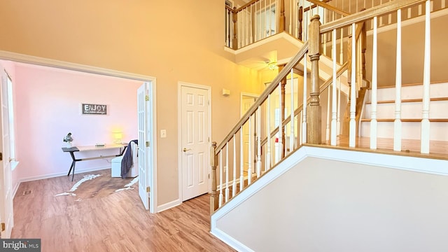 stairway featuring baseboards, a high ceiling, and wood finished floors