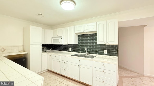 kitchen with white microwave, tile countertops, light tile patterned flooring, white cabinetry, and a sink