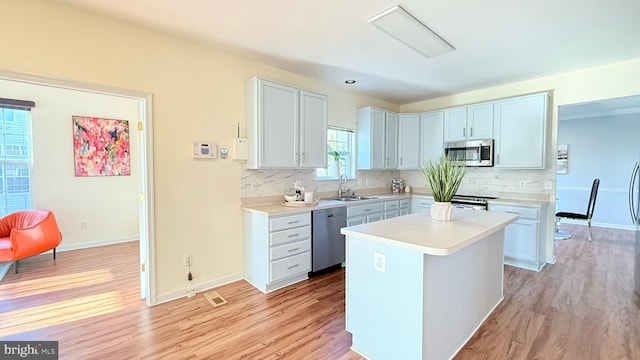 kitchen featuring light wood-style flooring, a sink, light countertops, appliances with stainless steel finishes, and tasteful backsplash