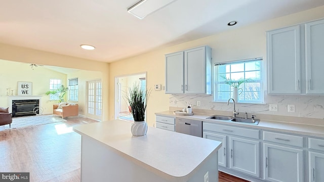 kitchen featuring open floor plan, light countertops, dishwashing machine, a fireplace, and a sink