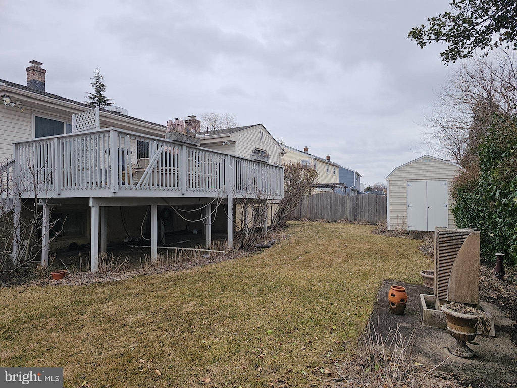 view of yard featuring a storage unit, a wooden deck, fence, and an outbuilding