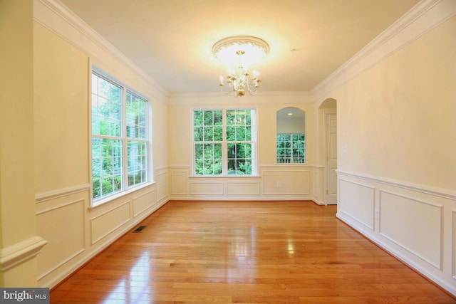 unfurnished room featuring visible vents, ornamental molding, light wood-type flooring, a decorative wall, and a notable chandelier