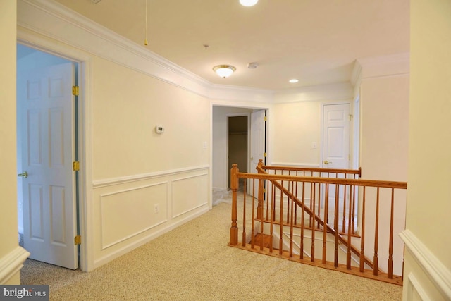 hallway with carpet, ornamental molding, a decorative wall, and an upstairs landing