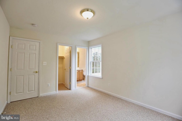 unfurnished bedroom featuring baseboards, light colored carpet, ensuite bathroom, a spacious closet, and a closet