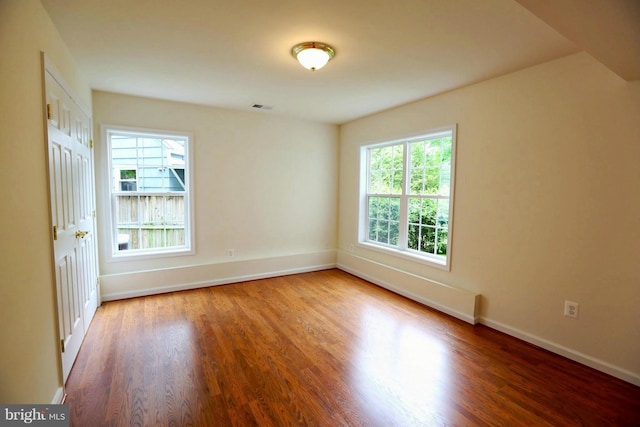 unfurnished room featuring wood finished floors, visible vents, and baseboards