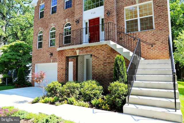 view of front of house with a garage, brick siding, driveway, and stairway