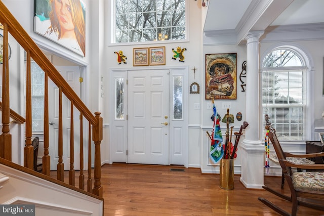 entrance foyer with wood finished floors, visible vents, stairs, ornamental molding, and ornate columns