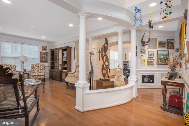 interior space featuring ornate columns, ornamental molding, a decorative wall, and wood finished floors